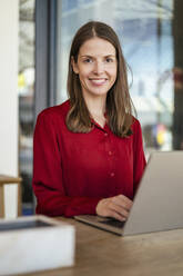 Smiling businesswoman with laptop at desk in office - DIGF18475