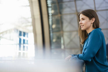 Thoughtful businesswoman leaning on railing in corridor - DIGF18483