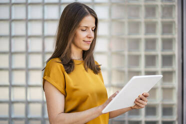 Businesswoman working on tablet PC by wall in office - DIGF18491