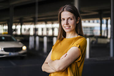 Smiling businesswoman with arms crossed in parking lot - DIGF18504