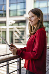 Thoughtful businesswoman with tablet PC standing by railing - DIGF18517