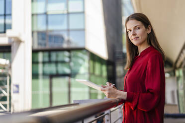 Selbstbewusste Geschäftsfrau mit Tablet-PC an einem Geländer am Arbeitsplatz - DIGF18519