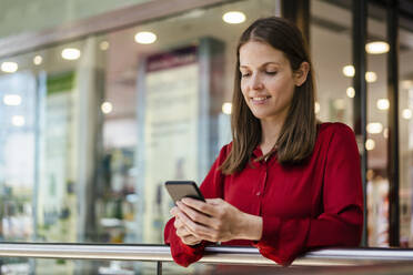 Geschäftsfrau, die im Büro eine Textnachricht über ihr Mobiltelefon verschickt - DIGF18520