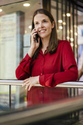 Lächelnde Geschäftsfrau, die im Bürokorridor mit ihrem Smartphone telefoniert - DIGF18521