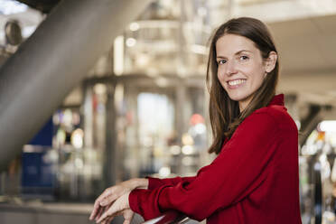 Smiling businesswoman leaning on railing in office - DIGF18524