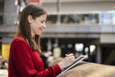 Lächelnde Geschäftsfrau, die einen digitalisierten Stift auf einem Tablet-PC am Arbeitsplatz benutzt - DIGF18525