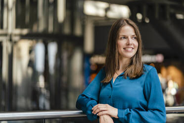 Thoughtful smiling businesswoman by railing at workplace - DIGF18540