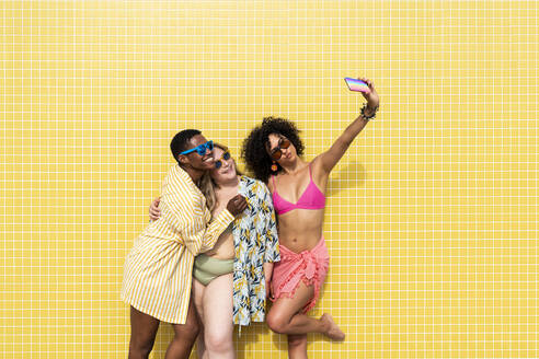 Multirassische Frauen machen ein Selfie mit ihrem Handy vor einer gelben Wand - OIPF02177