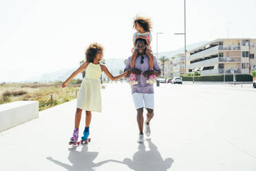 Happy girl roller skating by father carrying sister on shoulders - OIPF02191