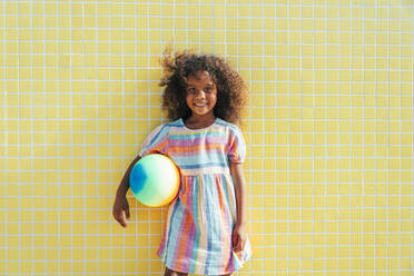 Nettes Mädchen mit Strandball an einem sonnigen Tag vor einer Wand stehend - OIPF02203