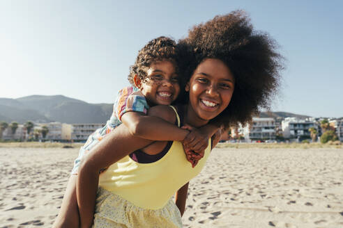 Happy girl piggybacking sister at beach - OIPF02226