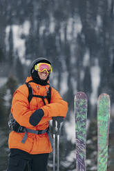 Lächelnder Mann in warmer Kleidung mit Skiern und Stöcken - OMIF01014
