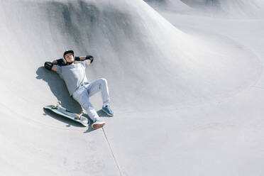Mann mit Skateboard entspannt sich im Skatepark an einem sonnigen Tag - OMIF01016