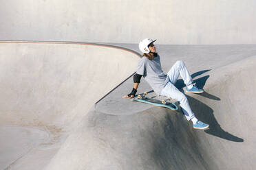 Nachdenklicher Mann sitzt mit Skateboard in Skatepark - OMIF01032