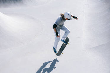 Skateboarder doing stunt with skateboard on sunny day - OMIF01035