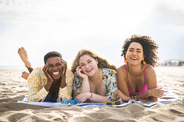 Glückliche gemischtrassige Freunde liegen auf einer Picknickdecke am Strand - OIPF02239