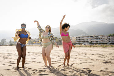 Group of young women dancing together in bikinis. Happy young women smiling  cheerfully while dancing in swimwear. Carefree female friends having fun  and enjoying their summer vacation at the beach. stock photo