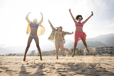 Carefree friends with arms raised jumping at beach on sunny day - OIPF02257