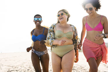 Üppige Frau mit Sonnenbrille läuft mit Freunden am Strand - OIPF02262