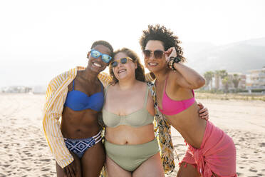Lächelnde Frauen mit Sonnenbrille und umschlungenen Armen am Strand - OIPF02264