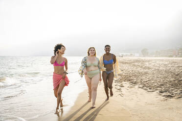 Gemischtrassige Frauen spazieren am Strand an einem sonnigen Tag - OIPF02281