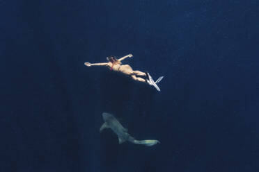 Woman swimming with shark in deep blue sea - KNTF06743