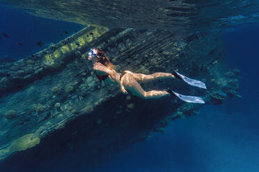 Woman swimming by shipwreck in sea - KNTF06748