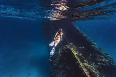 Woman wearing diving flippers swimming over shipwreck in sea - KNTF06751