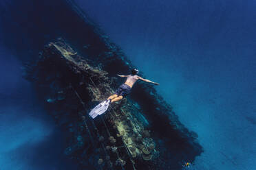 Man with arms outstretched swimming over shipwreck in sea - KNTF06757