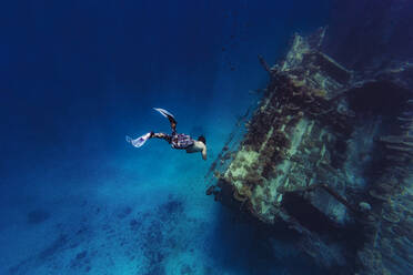 Man with diving flippers swimming towards shipwreck in sea - KNTF06759