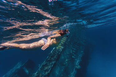 Woman swimming near shipwreck in sea - KNTF06761