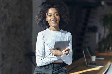 Lächelnde Geschäftsfrau mit Brille und Tablet-PC auf dem Schreibtisch im Büro - JSRF02163