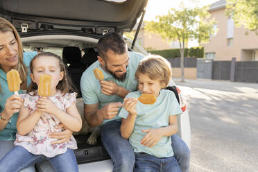 Glückliche Familie isst Eis auf dem Rücksitz eines Autos - JCCMF06785