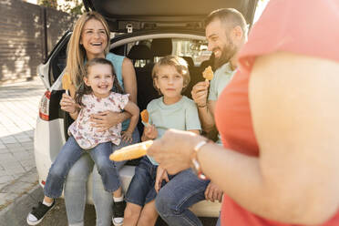 Happy family with ice pops sitting at back of car - JCCMF06791
