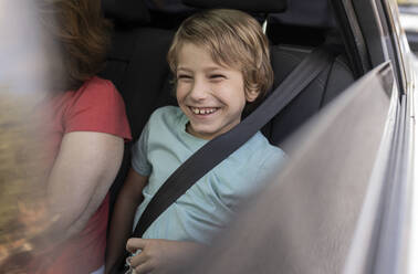 Smiling boy sitting by grandmother in car - JCCMF06799