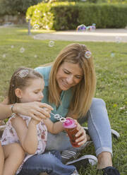 Smiling woman with daughter dipping bubble wand in bottle - JCCMF06810