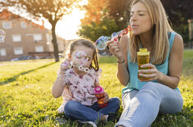 Mother and daughter blowing bubbles at park - JCCMF06811