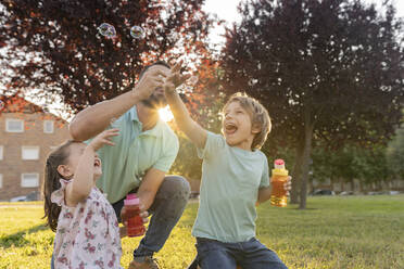 Mann bläst Seifenblasen mit Sohn und Tochter im Park - JCCMF06820