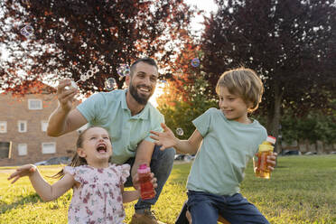 Kinder und Vater spielen mit Seifenblasen im Park - JCCMF06821