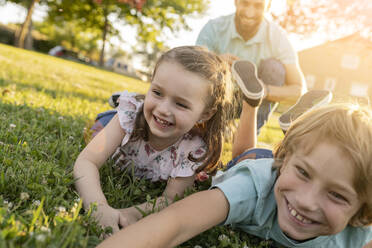 Glückliche Geschwister mit Vater im Park liegend - JCCMF06825