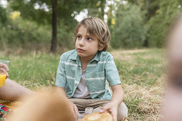Boy holding bread sitting at park - JCCMF06832