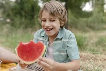 Smiling boy with watermelon slice sitting at park - JCCMF06836