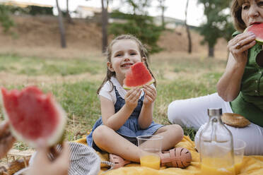 Cute girl holding watermelon sitting by grandmother - JCCMF06839