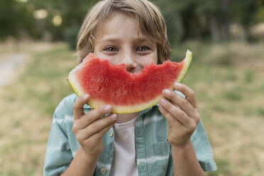 Boy holding slice of watermelon in front of face - JCCMF06843