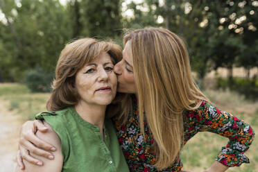 Loving daughter kissing mother at park - JCCMF06846