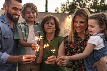 Smiling family burning sparklers together - JCCMF06857