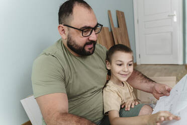 Smiling man with son reading instruction manual at home - OSF00533