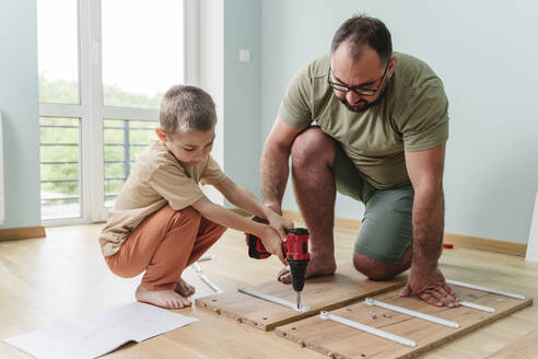 Father with son using drill on plank at home - OSF00535