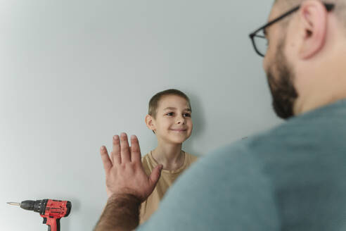 Lächelnder Junge gibt seinem Vater vor einer Mauer die Hand - OSF00542