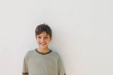 Smiling boy standing in front of white wall - IHF01046